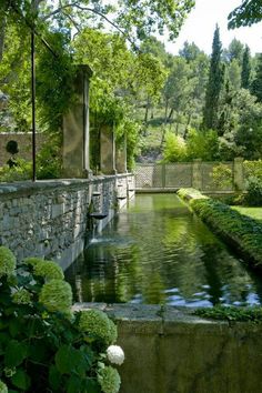 a small pond in the middle of a garden with stone walls and trees around it