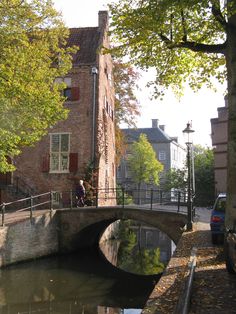 a man walking across a bridge over a small river next to tall brick buildings and trees