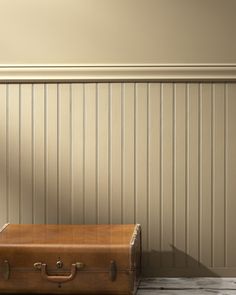 an old suitcase sitting on the floor in front of a wall with striped paneling