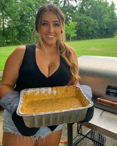 a woman holding a tray of food in front of an outdoor bbq with grass and trees