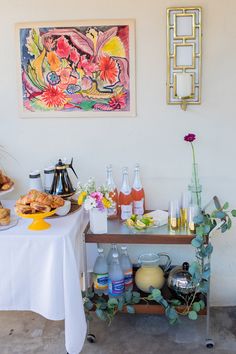 a table with food and drinks on it in front of a painting hanging on the wall