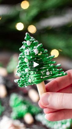 a hand is holding a small green christmas tree on a toothpick with white dots