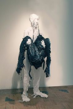 a white and black sculpture with plastic bags on it's back, sitting in front of a wall