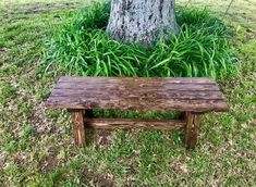 a wooden bench sitting next to a tree in the middle of a grass covered field