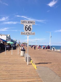 a sign that is on the side of a wooden pier near the ocean with people walking around