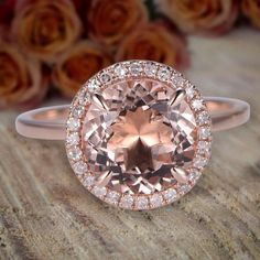 an oval cut peach morganite surrounded by white diamonds on a wooden surface with roses in the background