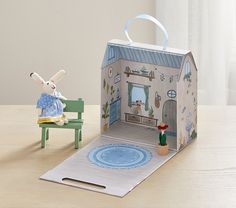 a paper dollhouse with a rabbit sitting on a chair next to it and a toy house in the background