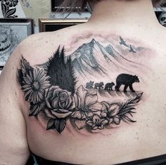 a woman with a bear and flowers tattoo on her upper back shoulder, in front of a mountain scene