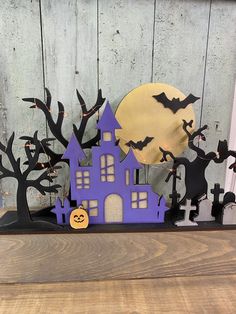 a purple house with bats and pumpkins in front of it on a wooden table