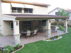 a patio with chairs and tables in front of a house that has grass on the ground