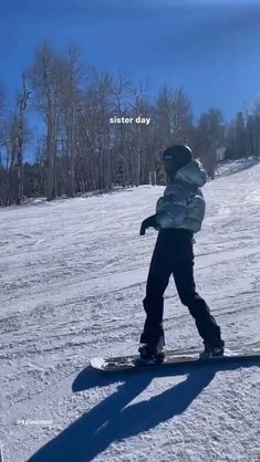 a person riding a snowboard down a snow covered slope with trees in the background