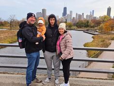 three adults and one child posing for a photo in front of a river with the city skyline behind them