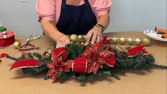 an older woman decorating a christmas wreath with poinsettis and ornaments on a table