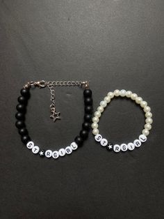 two bracelets with black beads and white pearls are on a dark surface, one has a silver star