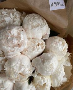 a bouquet of white peonies in a brown paper bag on top of a table