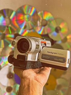 a person holding up a video camera in front of cd's and cds on the wall