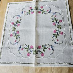 an open book with embroidered flowers on it sitting on a wooden table next to a pair of scissors