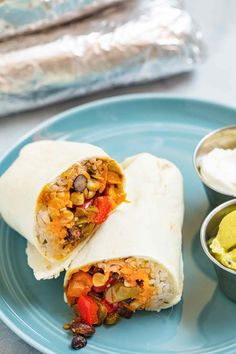 a burrito cut in half on a blue plate with guacamole and salsa