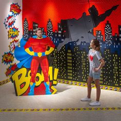 a girl standing in front of a wall with batman artwork on it and another woman looking at her