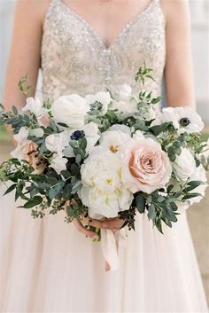 a bride holding a bouquet of white and pink flowers with greenery in her hands