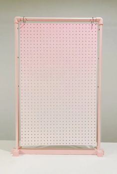 a pink pegboard with dots on it sitting in front of a gray wall and floor