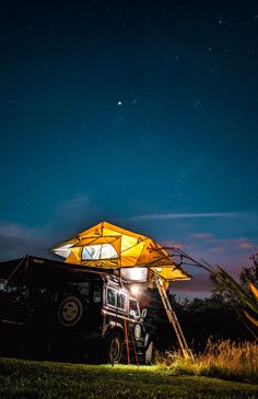 a truck parked under a yellow tent on the side of a road at night with stars in the sky