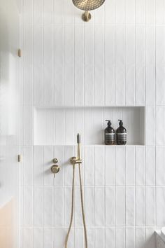 a white tiled bathroom with gold fixtures and shower faucet in the corner next to it