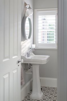 a white sink sitting under a bathroom mirror next to a window with shutters on it