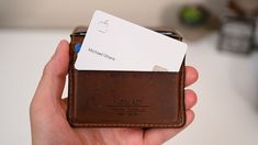 a hand holding a brown leather wallet with two credit cards in it