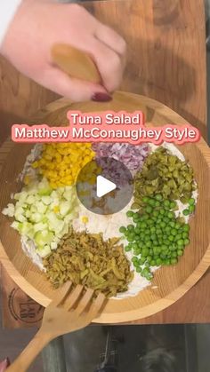 a wooden bowl filled with different types of food on top of a table next to a person holding a spatula