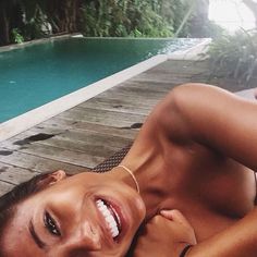 a woman laying on top of a wooden deck next to a pool with her arms around her chest