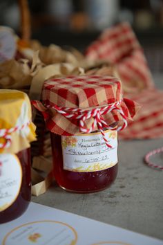 two jars of jam sitting on top of a table next to some paper and twine