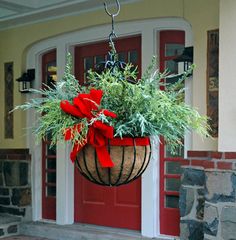 a hanging planter filled with greenery on the front steps of a house that is decorated for christmas