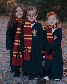 three young children dressed in harry potter robes and glasses, posing for the camera with their arms around each other