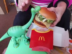 a person holding a hot dog in front of a toy dinosaur