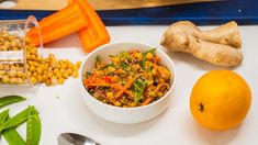 a white bowl filled with food next to an orange and some other vegetables on a table