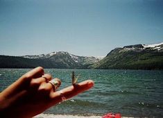 a hand reaching out towards the water with mountains in the background