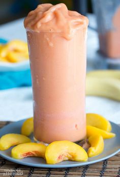 a glass filled with liquid sitting on top of a plate next to sliced peaches