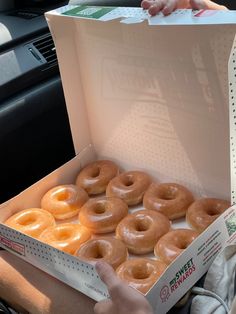 a person holding a box full of doughnuts in the back seat of a car