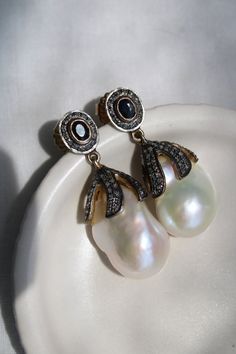 This is an incredible one-of-a-kind find with these Victorian pearl earrings, a true testament to timeless elegance and sophisticated craftsmanship. Each earring boasts a lustrous baroque pearl nestled within a setting of silver-topped gold, adorned with high domed rose cut diamonds that catch the light for a subtle, enchanting shimmer. The center stones, one a deep black onyx and the other a rich blue sapphire, hint at their possible origins as a bridal accessory, adding a touch of romantic his