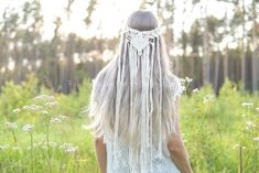 a woman with long white hair walking through the grass wearing a head piece made out of fringes