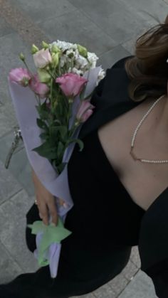 a woman in a black dress holding a bouquet of flowers on her left hand and looking at the camera