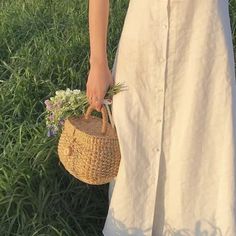 a woman in white dress holding a basket with flowers on it and grass behind her