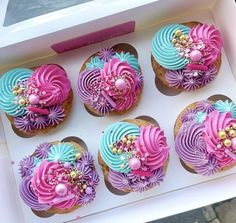 six decorated cupcakes sitting in a box on the ground with pink, blue and purple frosting