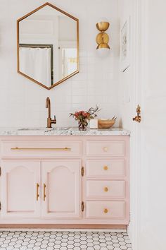 a bathroom with pink vanity, gold mirror and hexagonal tiles on the floor