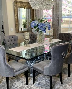 a dining room table and chairs with blue flowers in a vase on the glass top