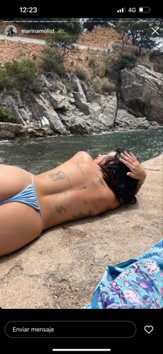 a woman laying on top of a beach next to a body of water with writing on her back