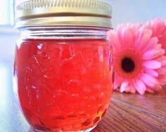 a jar filled with liquid sitting on top of a wooden table next to pink flowers