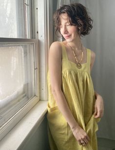 a woman standing next to a window in a yellow dress