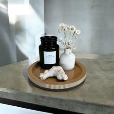 a white vase with flowers and a candle sitting on a wooden tray next to a dog bone